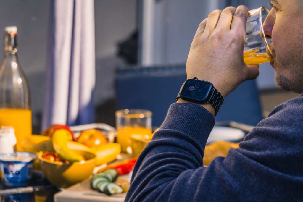 Férfi reggelizik gyümölcsöket és narancsitalt, Apple Watch-ot visel.