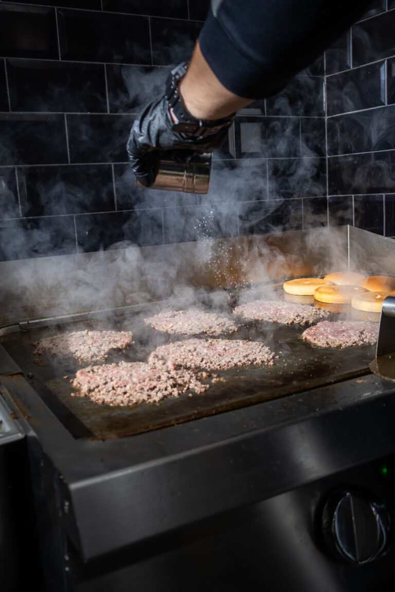 Hamburger hús darabok sütése sütőn, füstös konyhai környezetben.