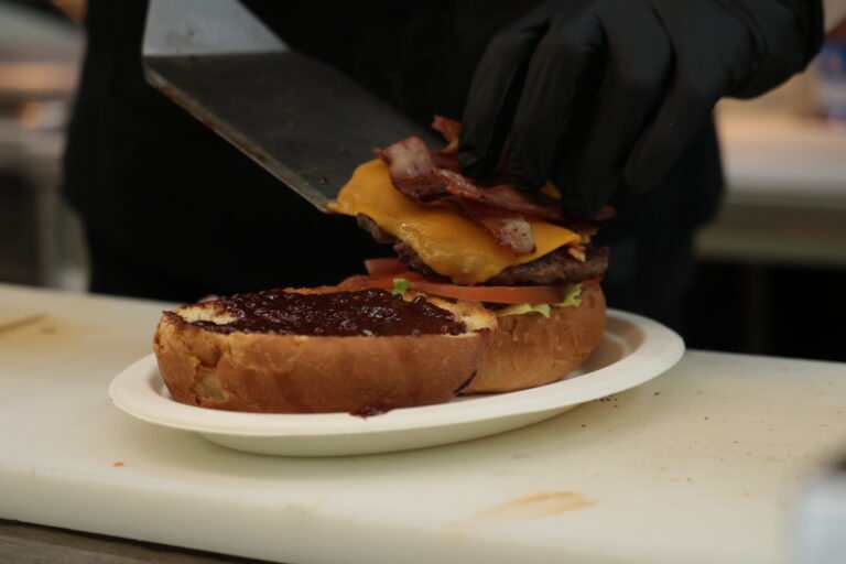 Főzőkéz egy húsos burger elkészítése fekete kesztyűben.